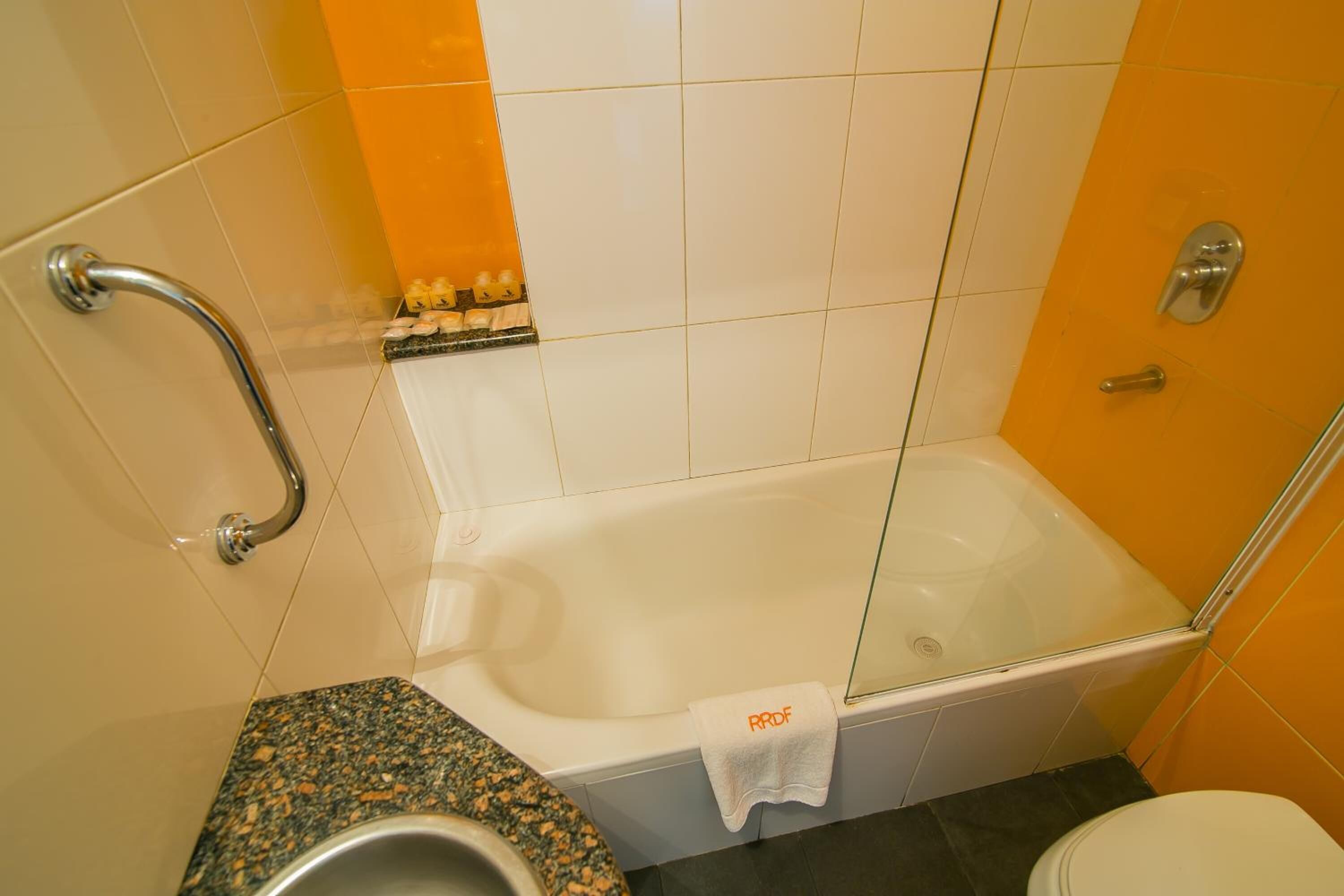 A bathroom with a bathtub, a toilet, and a handrail.