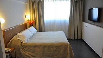 A hotel room with a bed, a television, and a window with curtains.