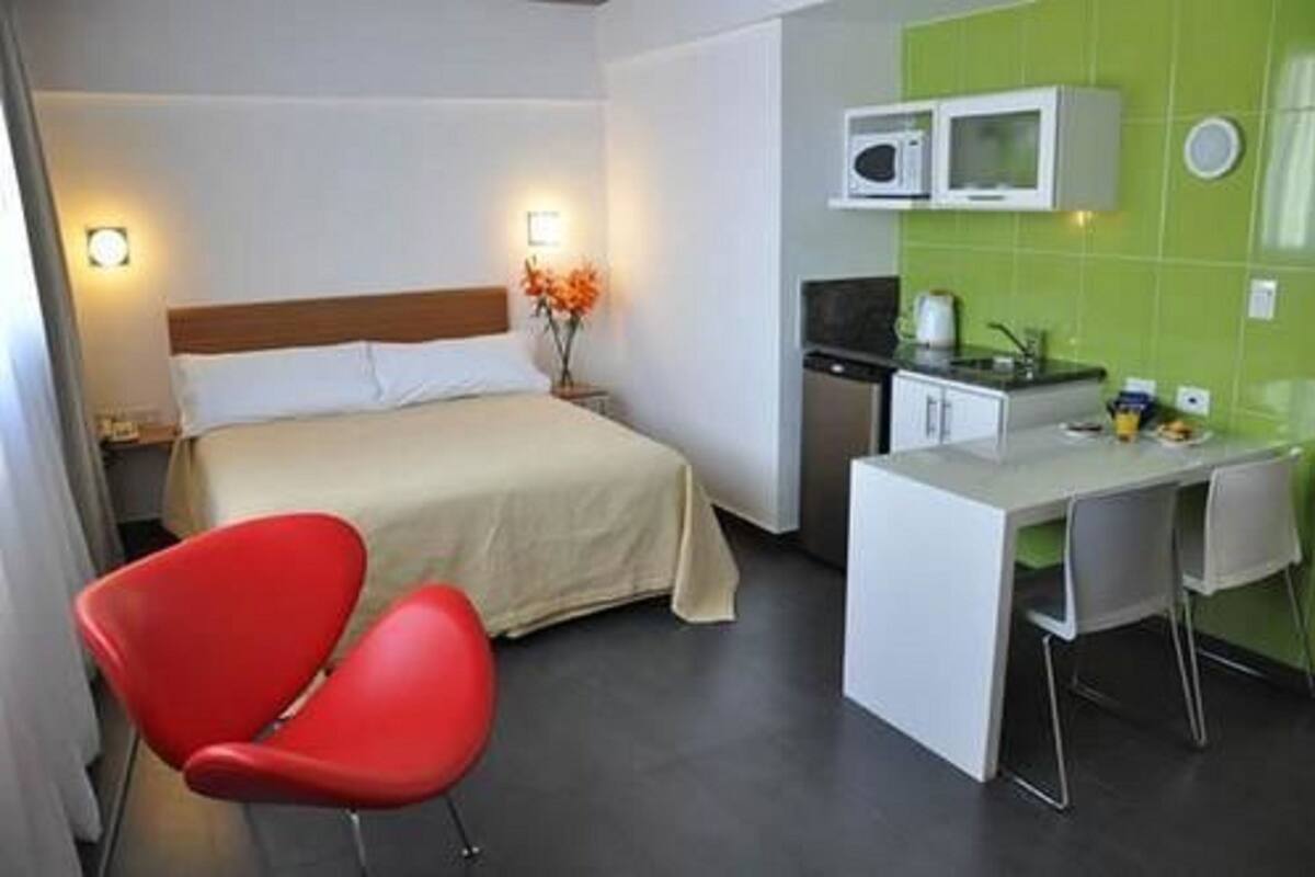 Een hotelkamer met een bed, een bureau, een rode stoel, een magnetron en een groene wand met tegels.