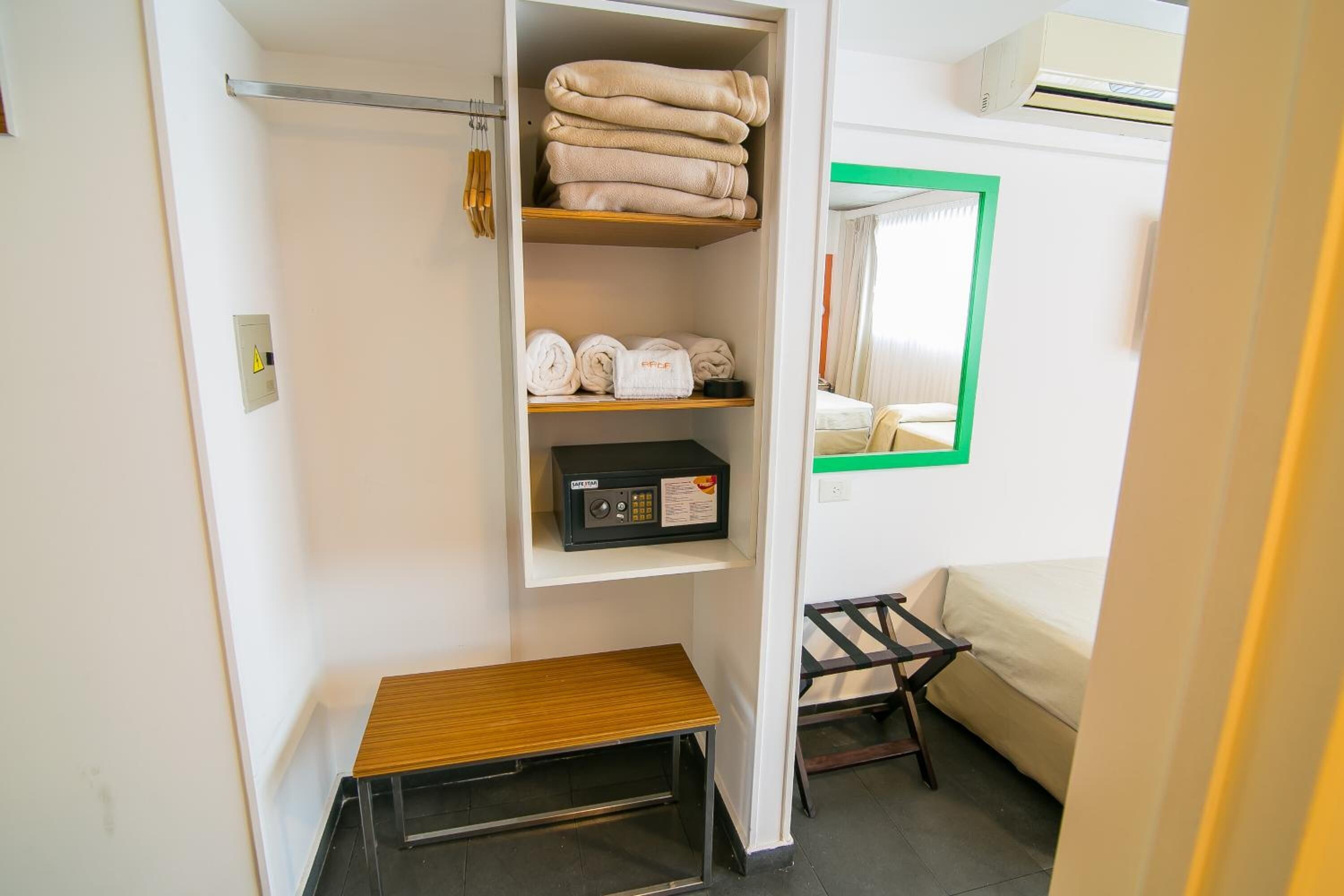 A hotel room with a bed, a shelf with towels, a small table, and a bedside table with a radio.