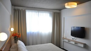 A hotel room with a bed, a TV mounted on the wall, a bedside table, and a window with curtains. - Roberta Rosa de Fontana Suites (Rosario)