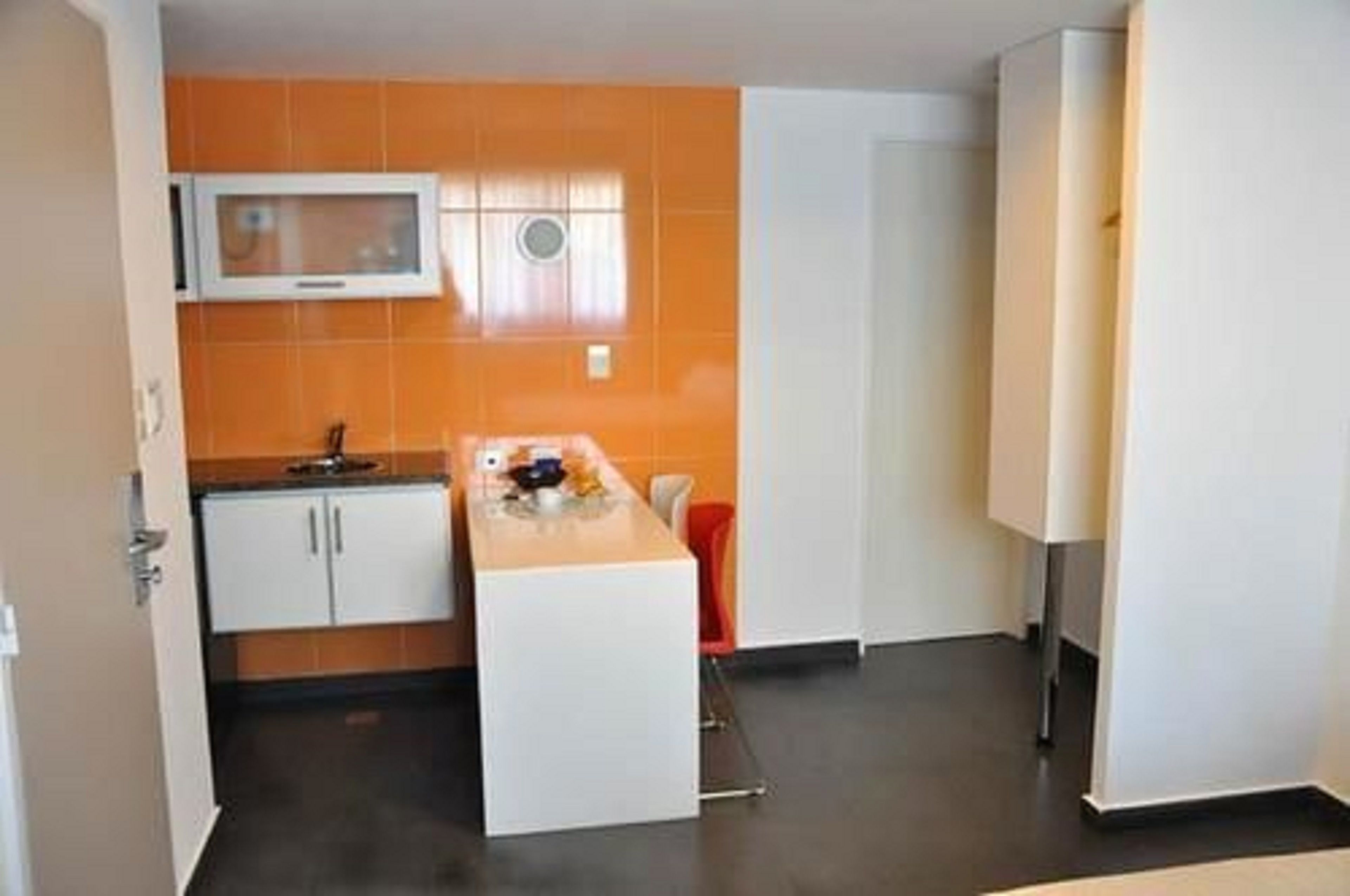 Une cuisine de taille réduite avec des carreaux orange, des armoires blanches et un four à micro-ondes.