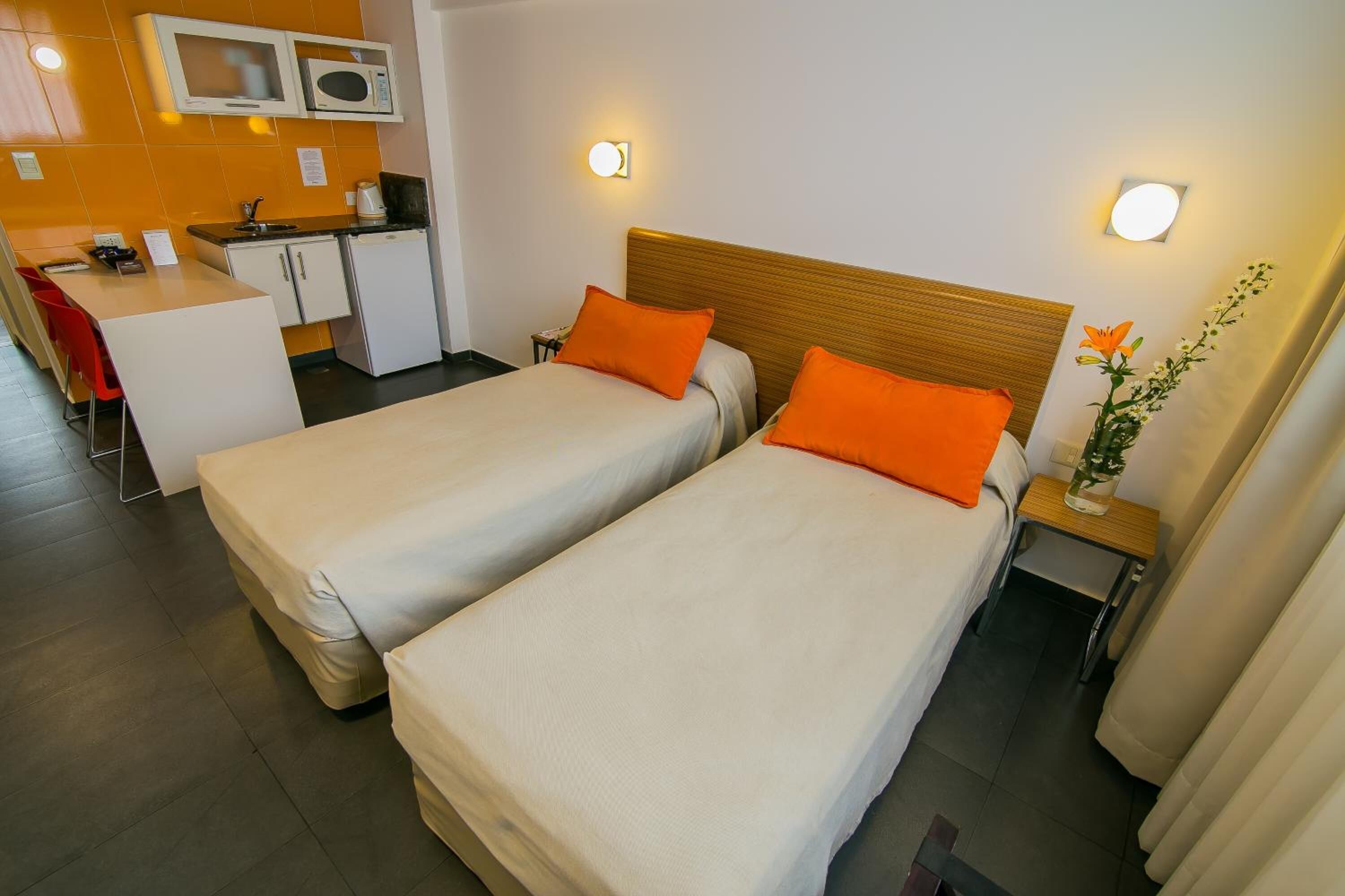 A hotel room with two beds, a kitchenette, a desk, and a small bathroom.