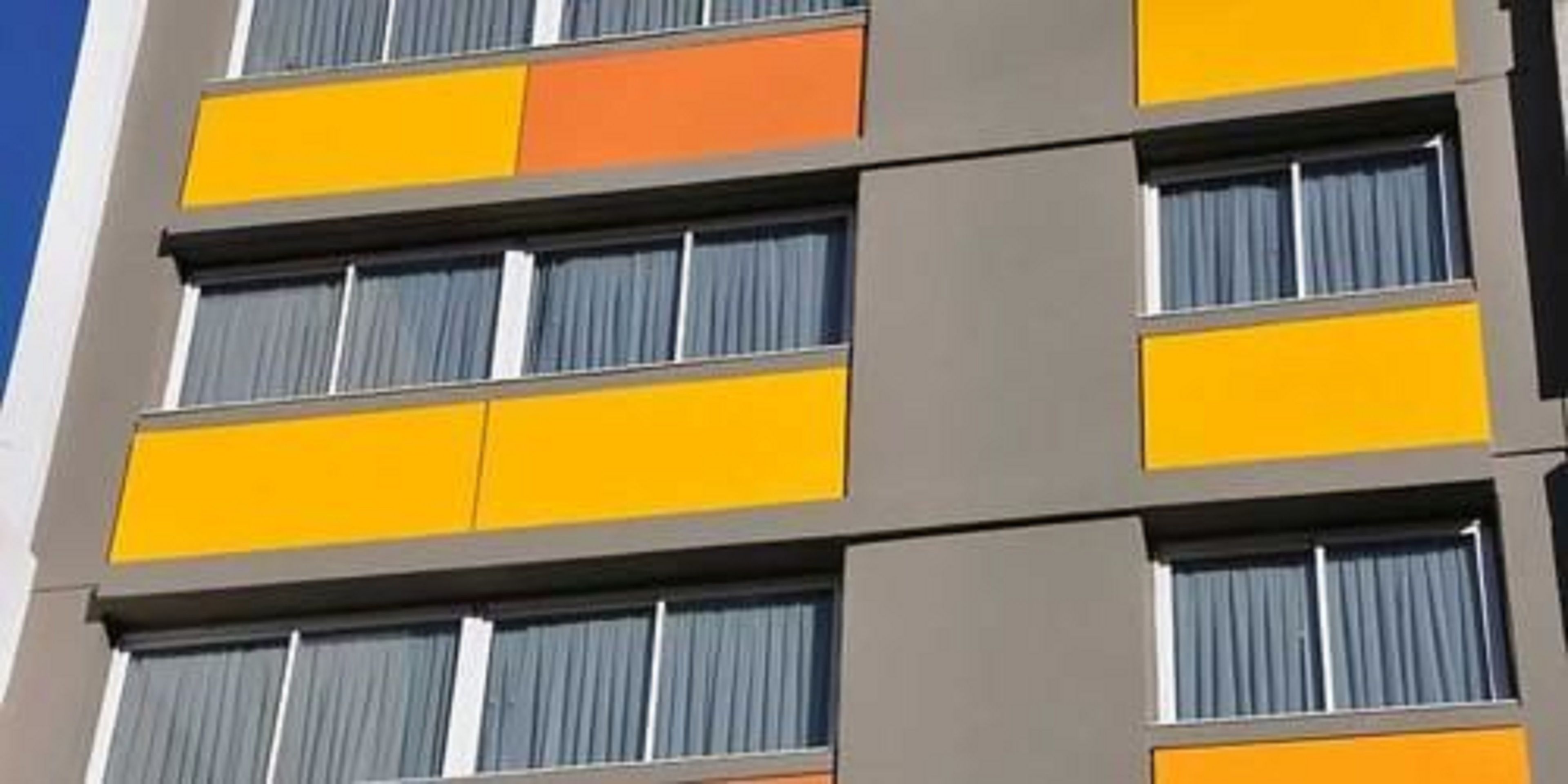 Un edificio de varios pisos con un diseño arquitectónico moderno, que presenta una serie de balcones con cortinas.