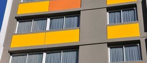 A multi-story building with a modern architectural design, featuring a series of balconies with curtains.