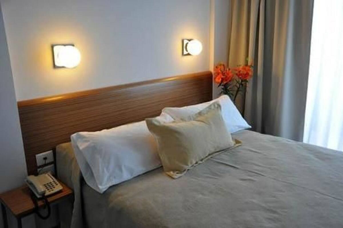 Hotelkamer met een houten hoofdeinde, een bed met witte lakens, een bedtelefoon en een vaas met bloemen.
