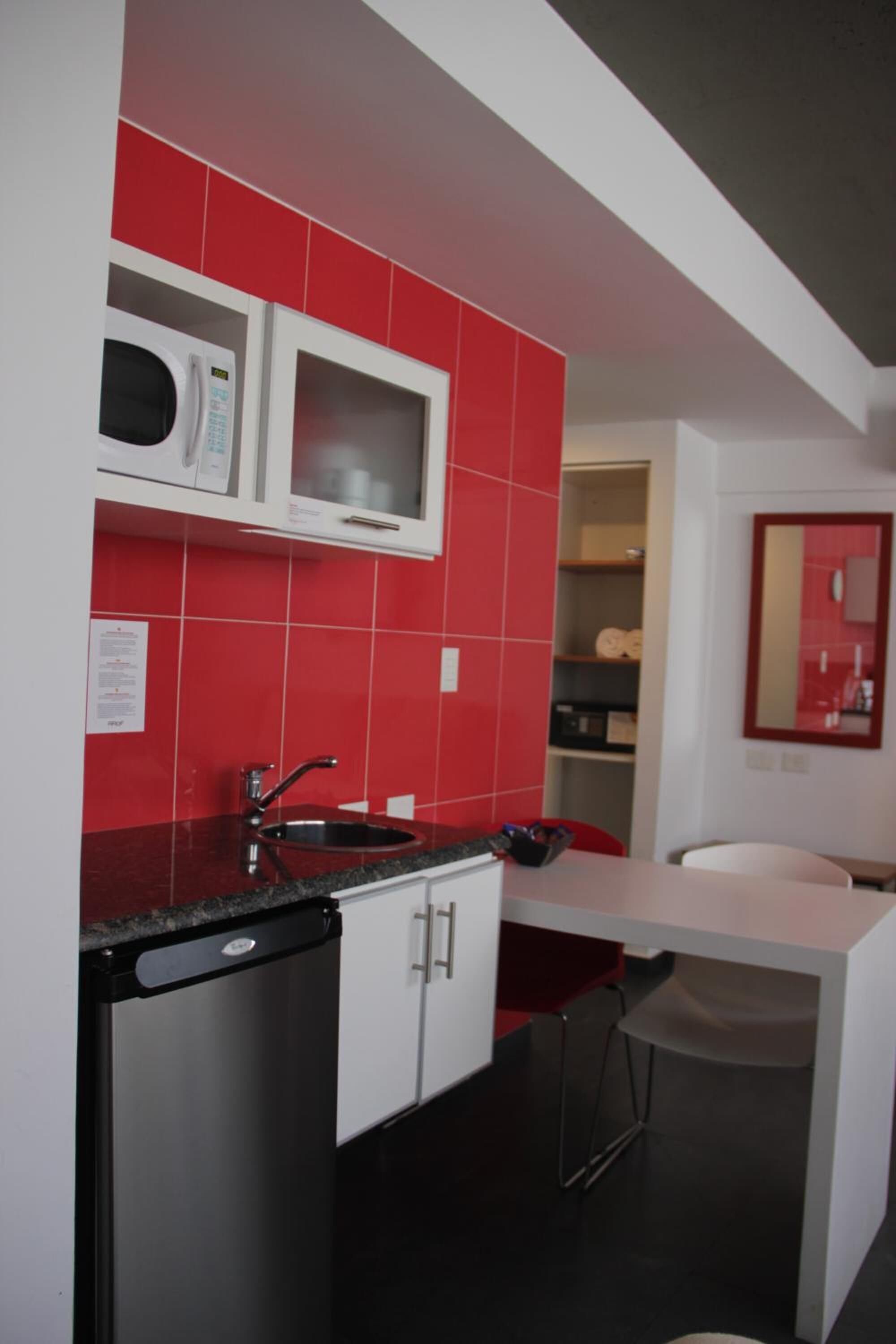 A compact kitchen with a microwave, sink, and a small dining area with a chair.