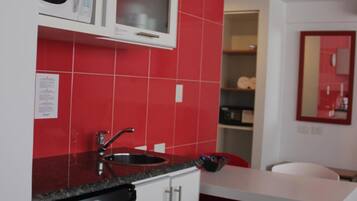 A compact kitchen with a microwave, sink, and a small dining area with a chair.