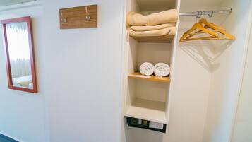 Una habitación de hotel con un armario blanco, una estantería de madera con toallas y un espejo en la pared.