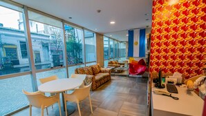 A modern hotel lobby with a large window, a reception desk, and a seating area with a patterned sofa and chairs. - Roberta Rosa de Fontana Suites (Rosario)