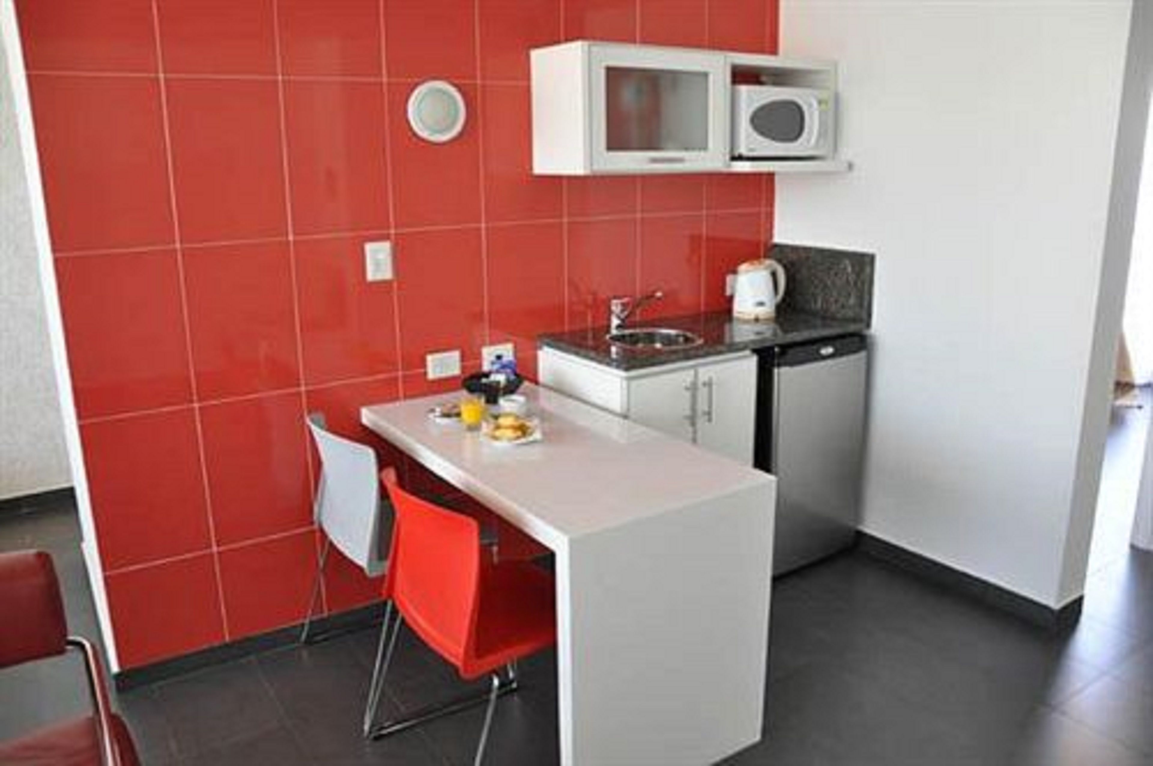 A compact kitchen with a white countertop, red chairs, and a microwave above the sink.