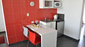 A compact kitchen with a white countertop, red chairs, and a microwave above the sink.