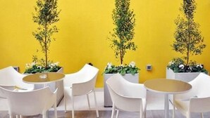 A yellow wall with three white planters containing green plants and white flowers. There are white chairs and a round table in the foreground. - Roberta Rosa de Fontana Suites (Rosario)