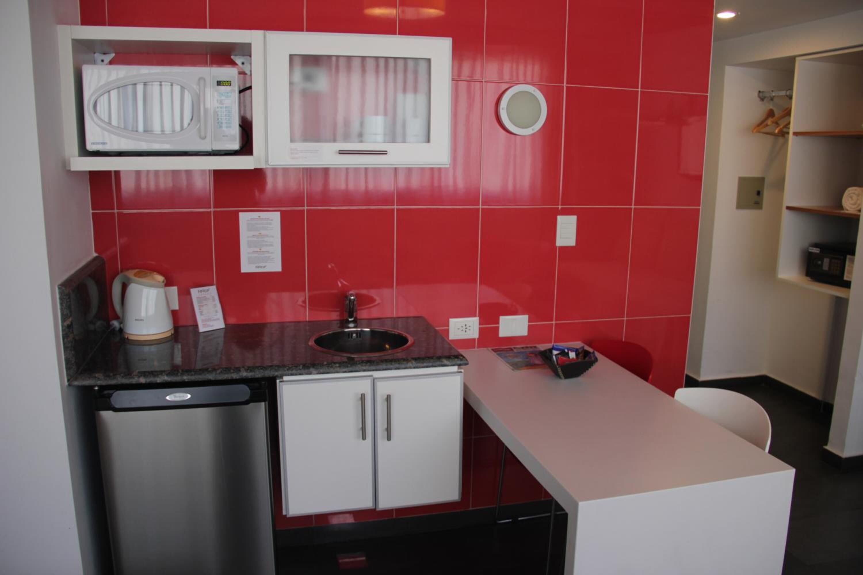 Cozinha compacta com micro-ondas, pia e pequena geladeira.