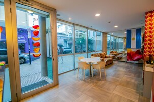 Un moderno vestíbulo de hotel con entrada de vidrio, un área de descanso con una mesa redonda y sillas, y vista a la calle.