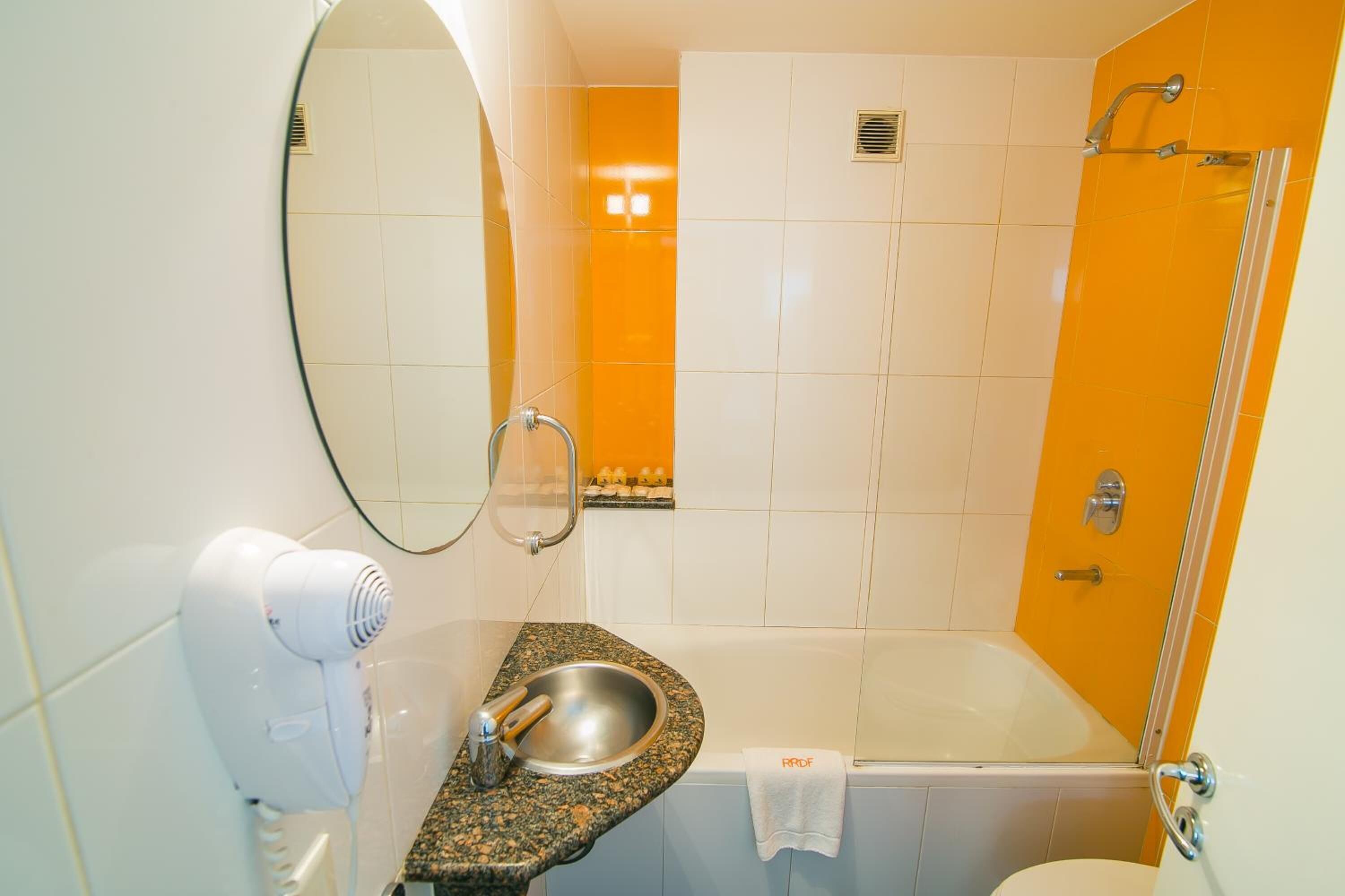 A bathroom with a sink, mirror, hairdryer, and a bathtub.