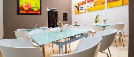 A modern conference room with glass tables and white chairs, featuring abstract paintings on the walls.