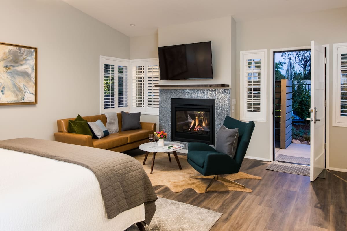 A modern bedroom with a fireplace, a bed, a sofa, and a TV.