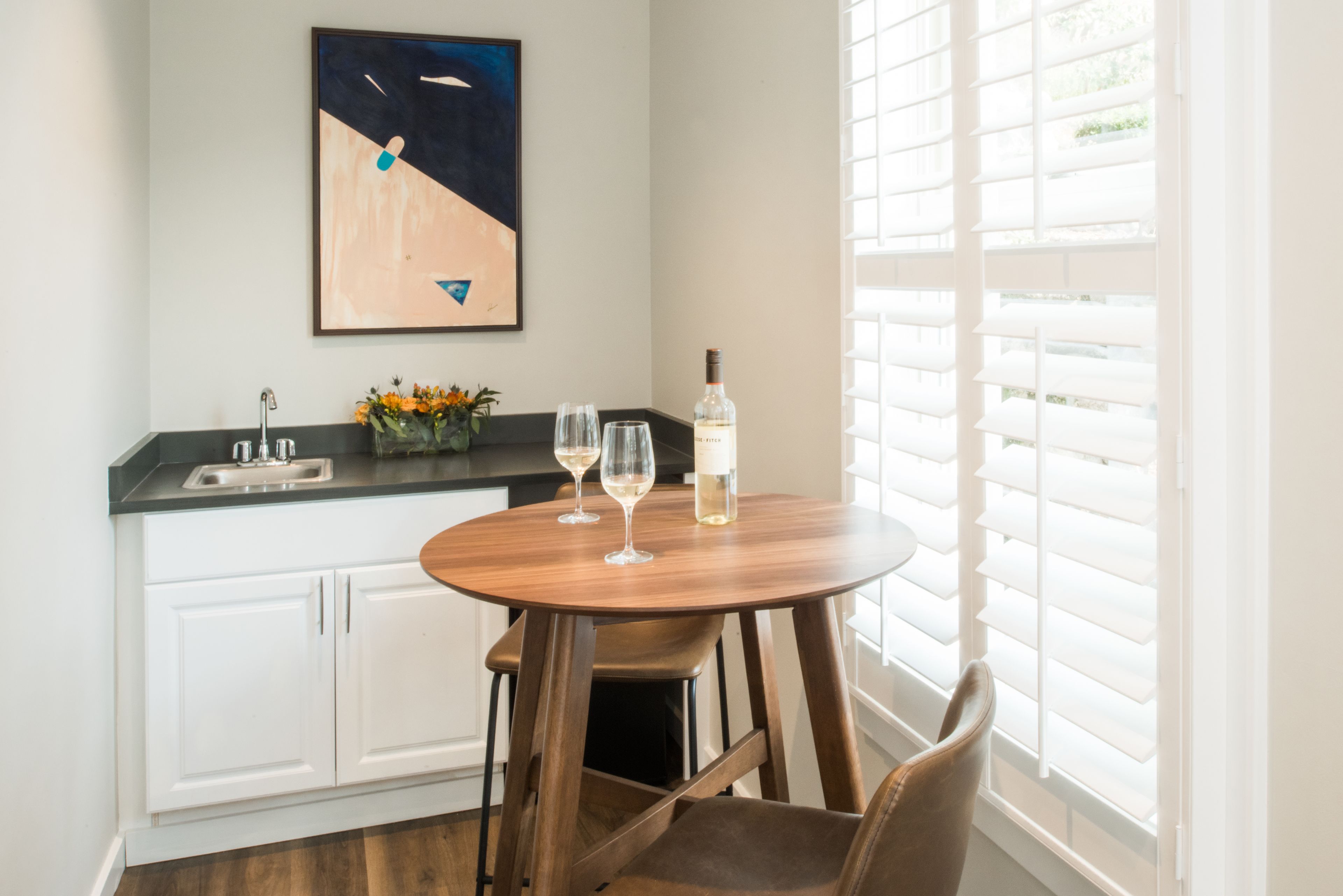 A kitchen with a round wooden table, two chairs, a wine bottle, and two wine glasses.