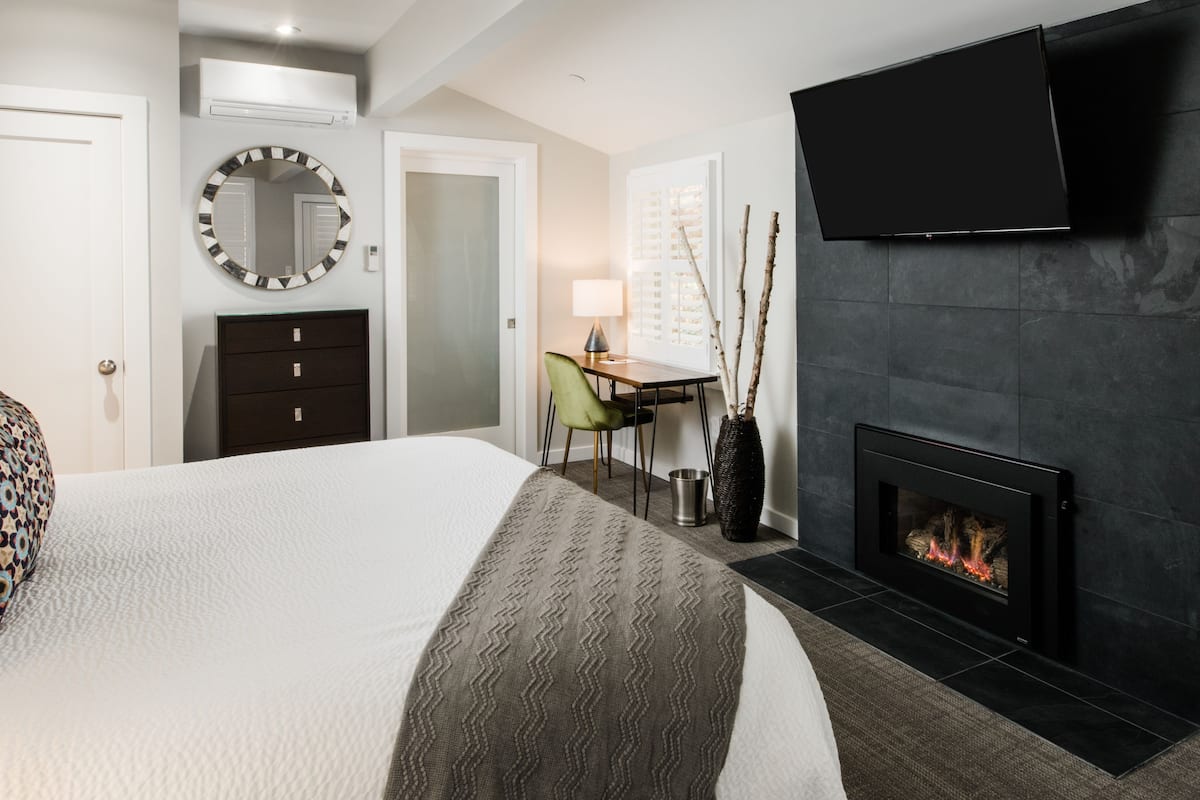 A hotel room with a large bed, a desk, a chair, a television, and a fireplace.