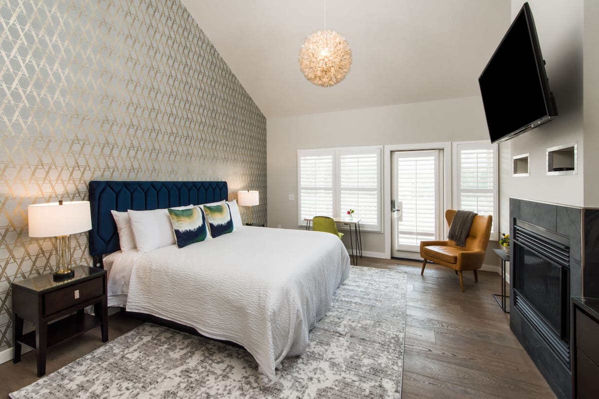 A bedroom with a bed, nightstands, a lamp, a chair, a television, and a fireplace.
