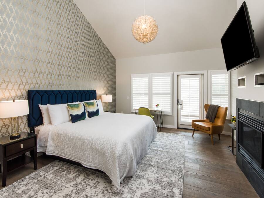 A bedroom with a bed, nightstands, a lamp, a chair, a television, and a fireplace.