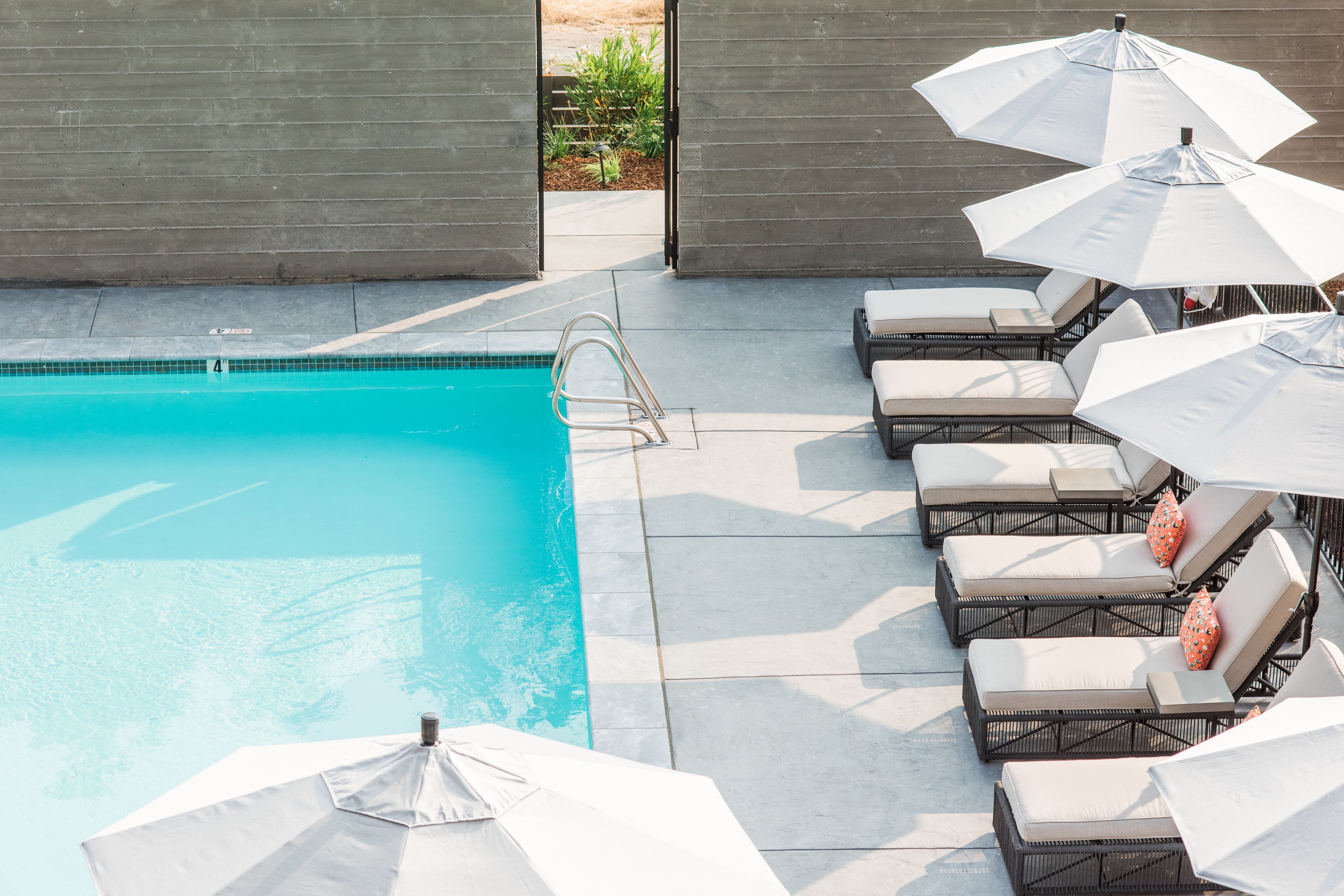 A pool area with a clear blue pool, a diving board, and several lounge chairs with umbrellas.