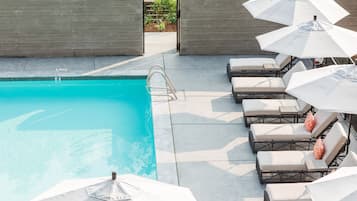 A pool area with a clear blue pool, a diving board, and several lounge chairs with umbrellas.