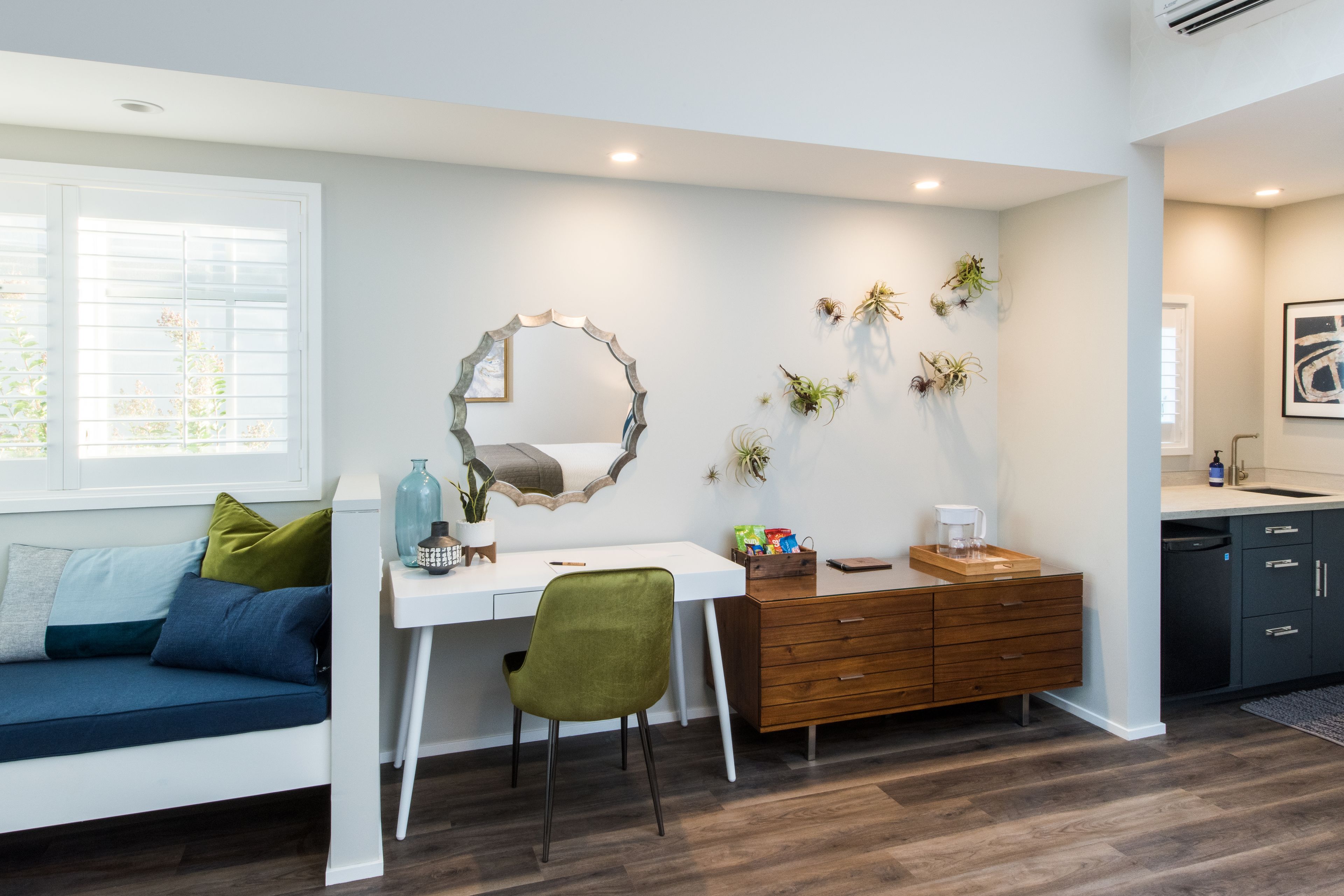 A modern living room with a white desk, green chair, and a sofa with blue cushions.