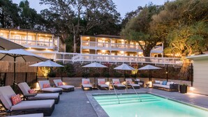 A pool area with lounge chairs and umbrellas, a two-story building with balconies, and a well-lit outdoor space. - Olea Hotel (Glen Ellen)