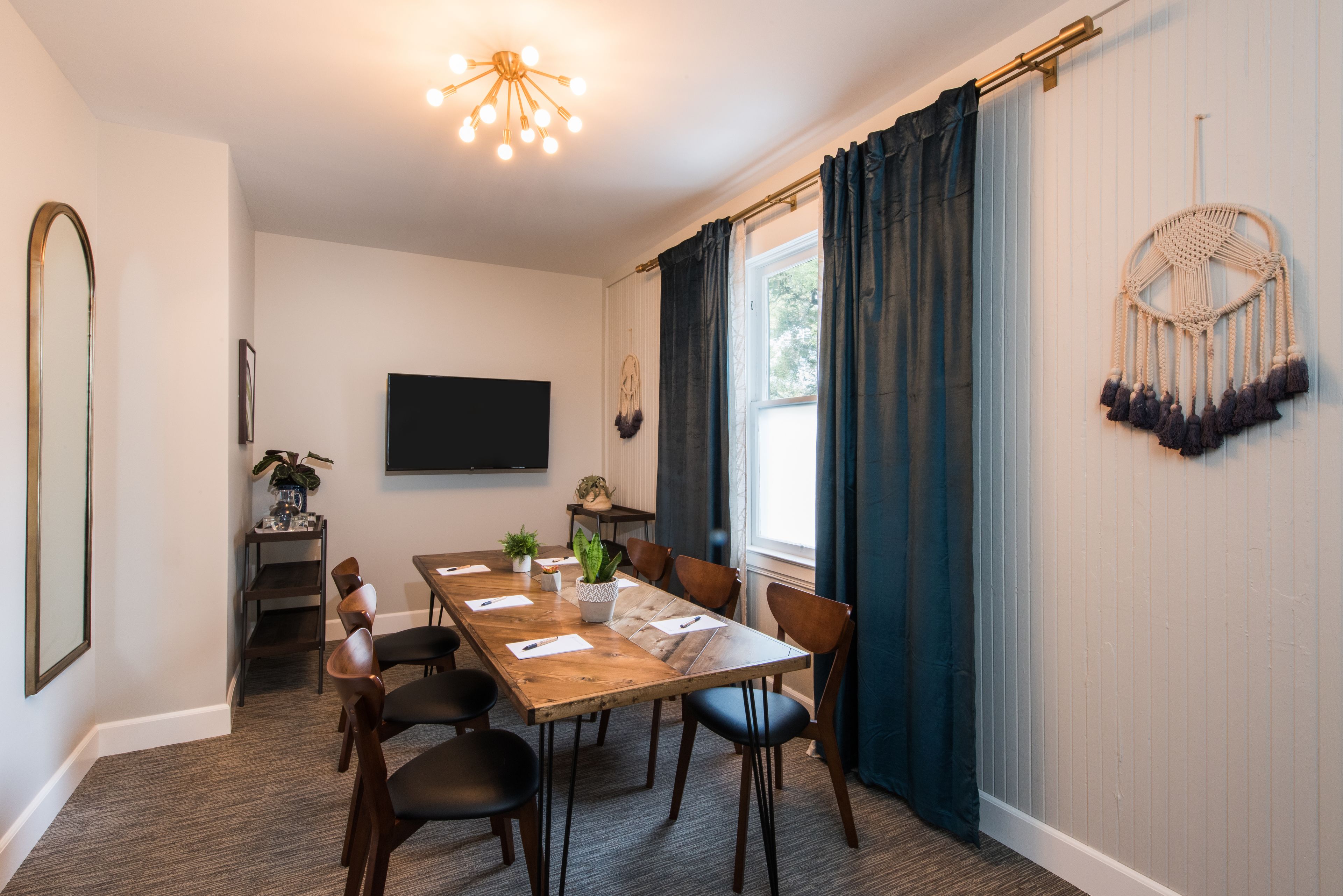 A dining area with a wooden table, chairs, a plant, and a wall-mounted television.