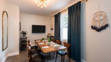 A dining area with a wooden table, chairs, a plant, and a wall-mounted television.