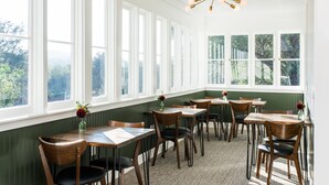 A dining area with multiple tables and chairs, large windows with a view of greenery, and a modern chandelier. - Olea Hotel (Glen Ellen)