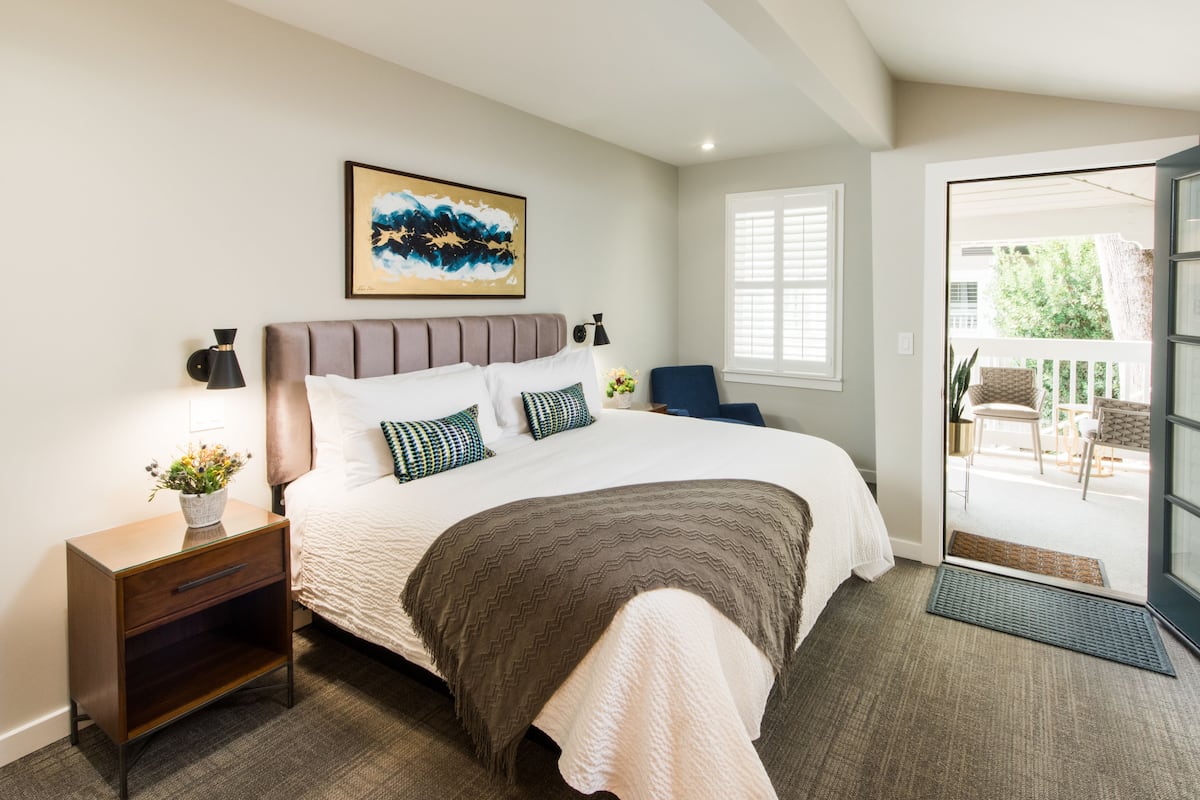 A bedroom with a bed, nightstand, lamp, and artwork.