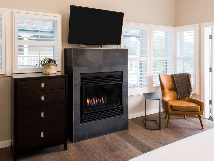 A modern living room with a fireplace, a television mounted above it, a leather armchair, and a potted plant.