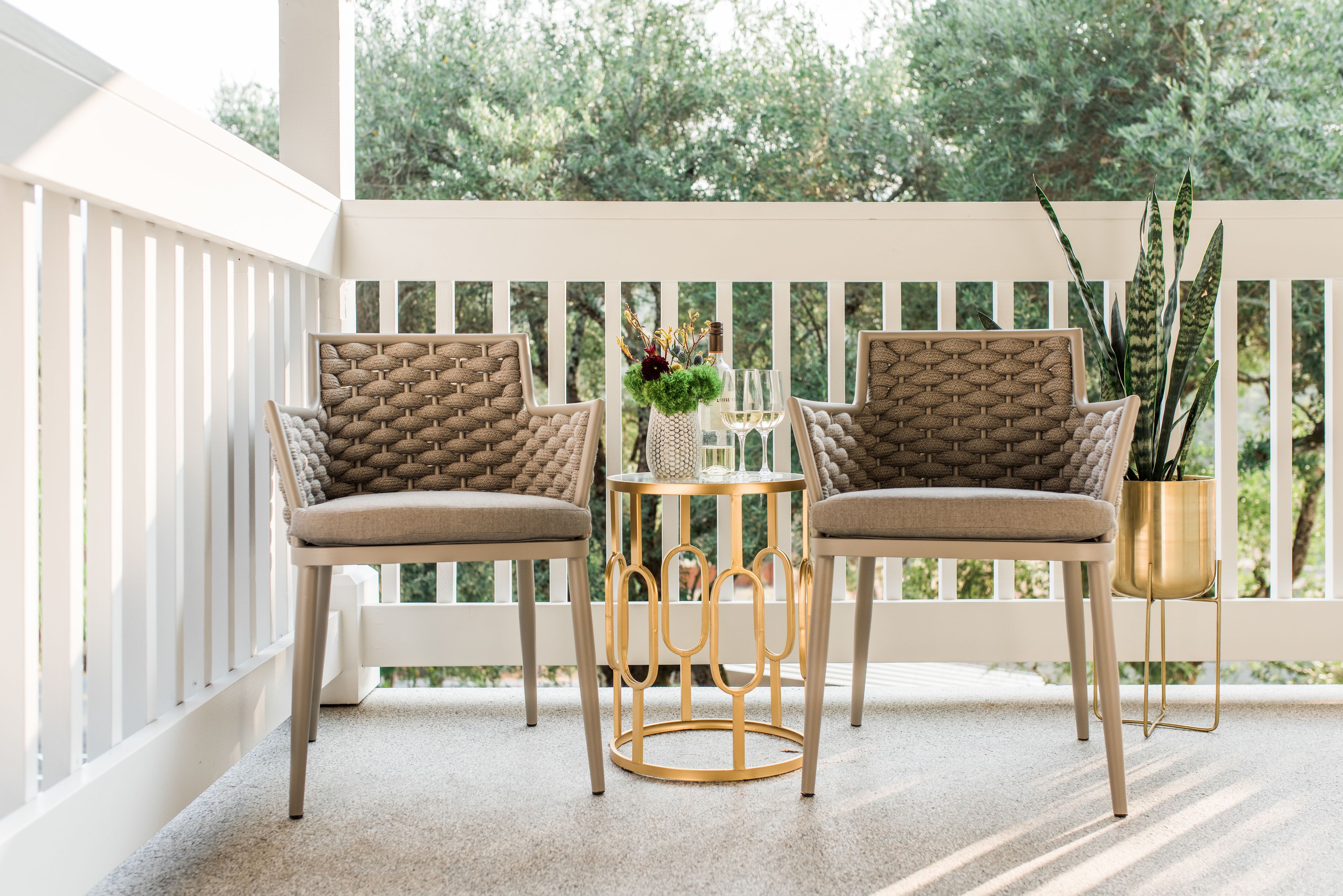 A balcony with two wicker chairs, a small round table, and a potted plant.