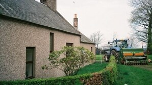 A stone building with a chimney, a small tree, and a tractor in the background. - Dykefield Farm B&B (Mauchline)