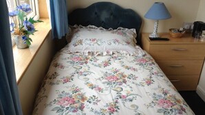 A bed with a floral bedspread, a blue lamp, and a window with flowers. - Dykefield Farm B&B (Mauchline)