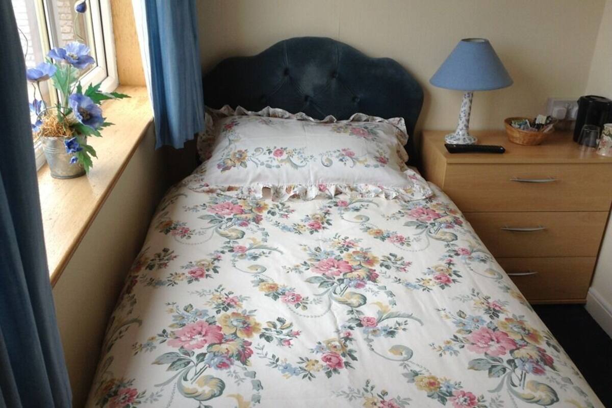 A bed with a floral bedspread, a blue lamp, and a window with flowers.