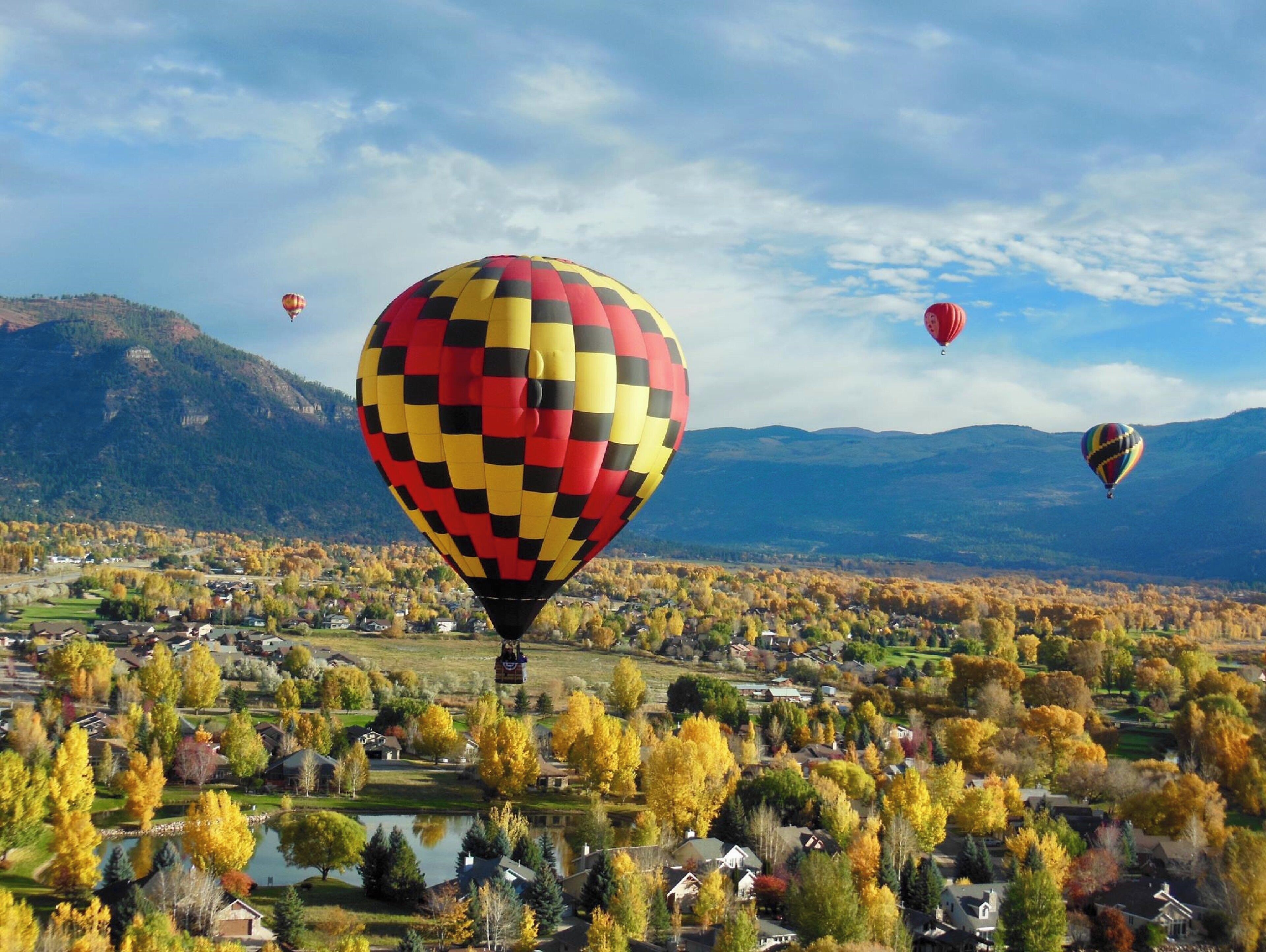 A hot air balloon over a residential area with autumn foliage and mountains in the background.