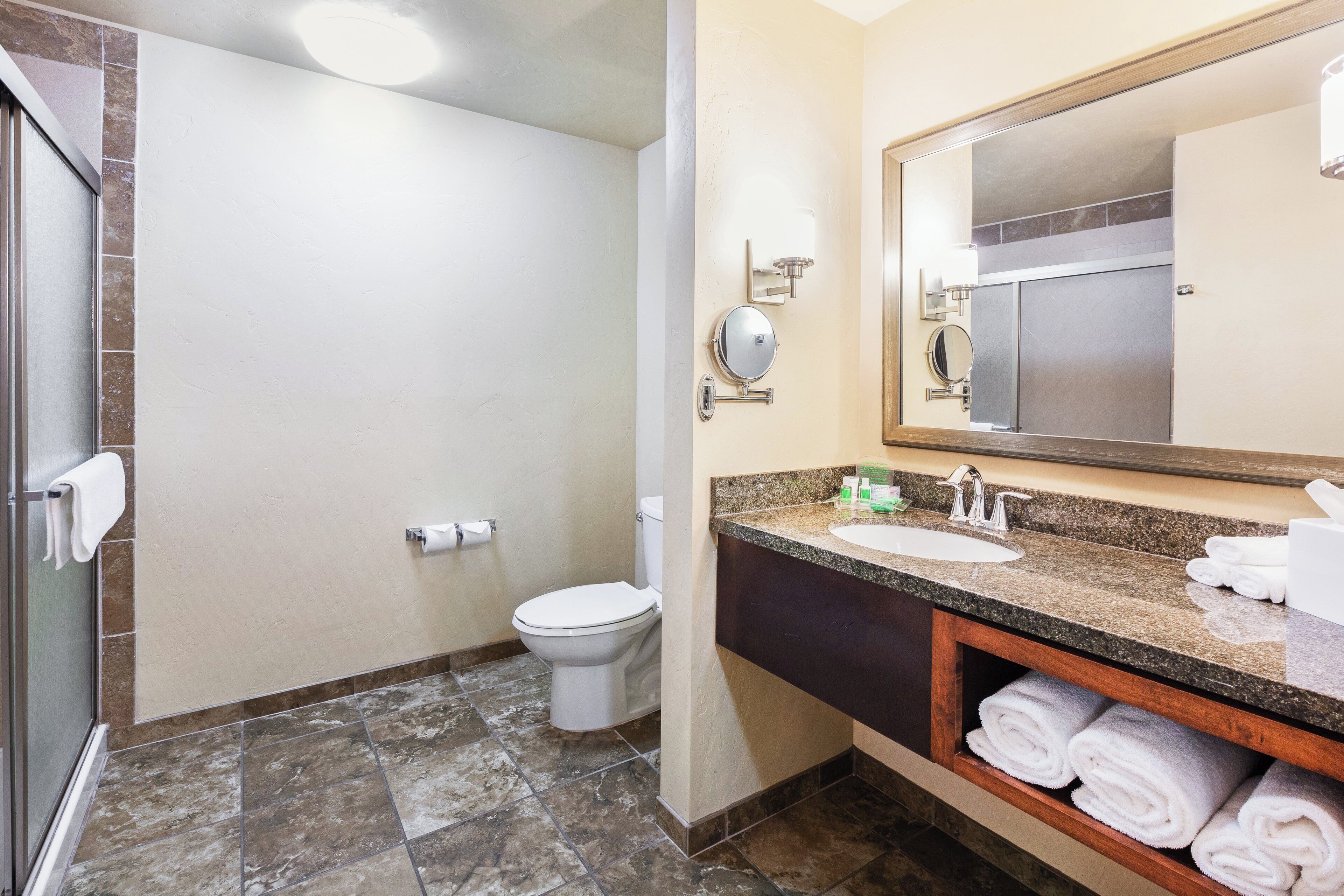 A bathroom with a shower, toilet, sink, and a mirror.