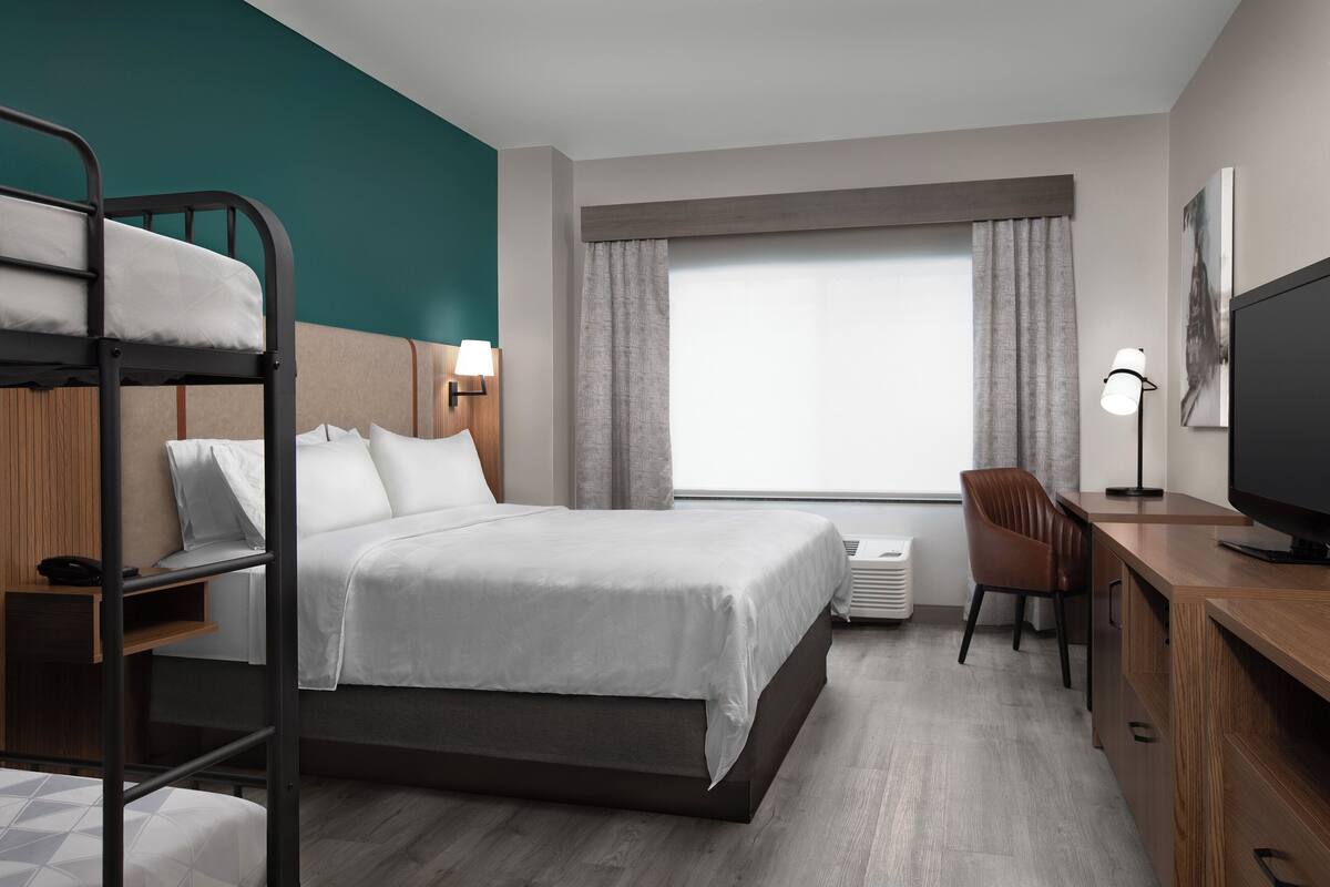 Una habitación de hotel con literas, un escritorio con una silla, un televisor y una ventana con cortinas.