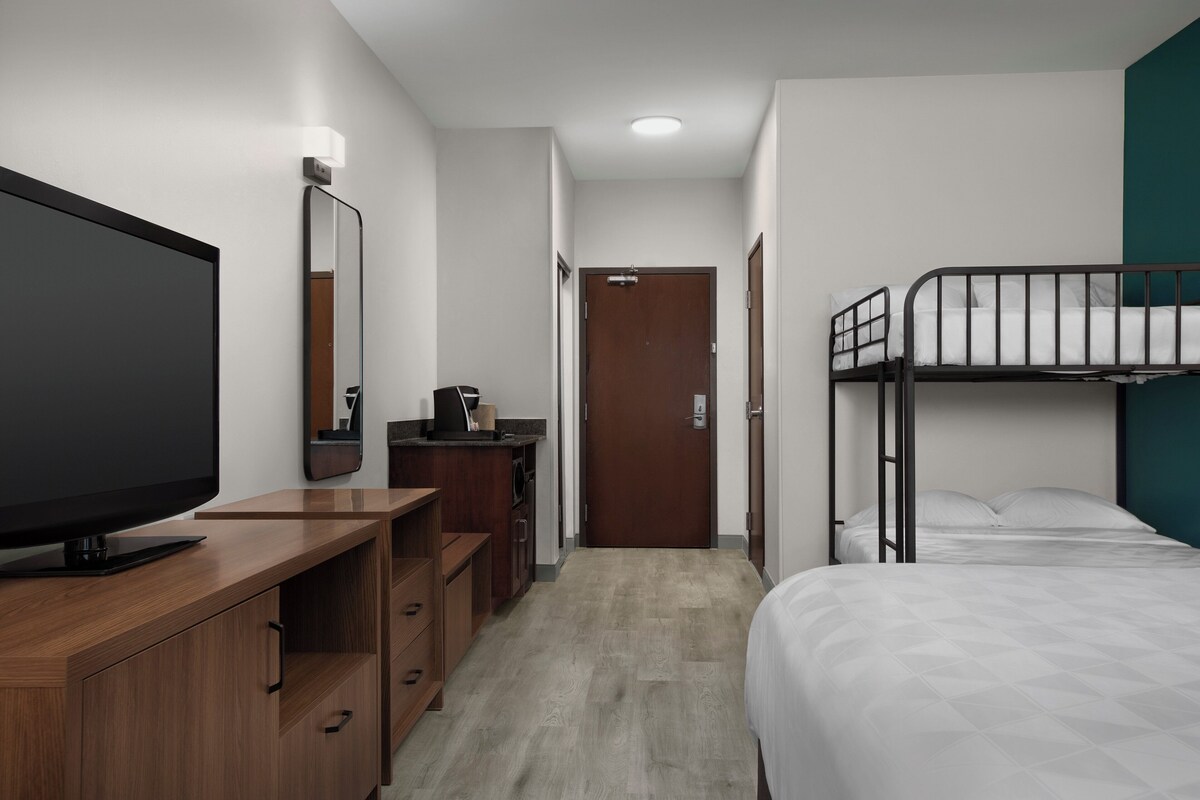 Ein Hotelzimmer mit Fernseher, Holzschreibtisch, Kommode und Etagenbett.