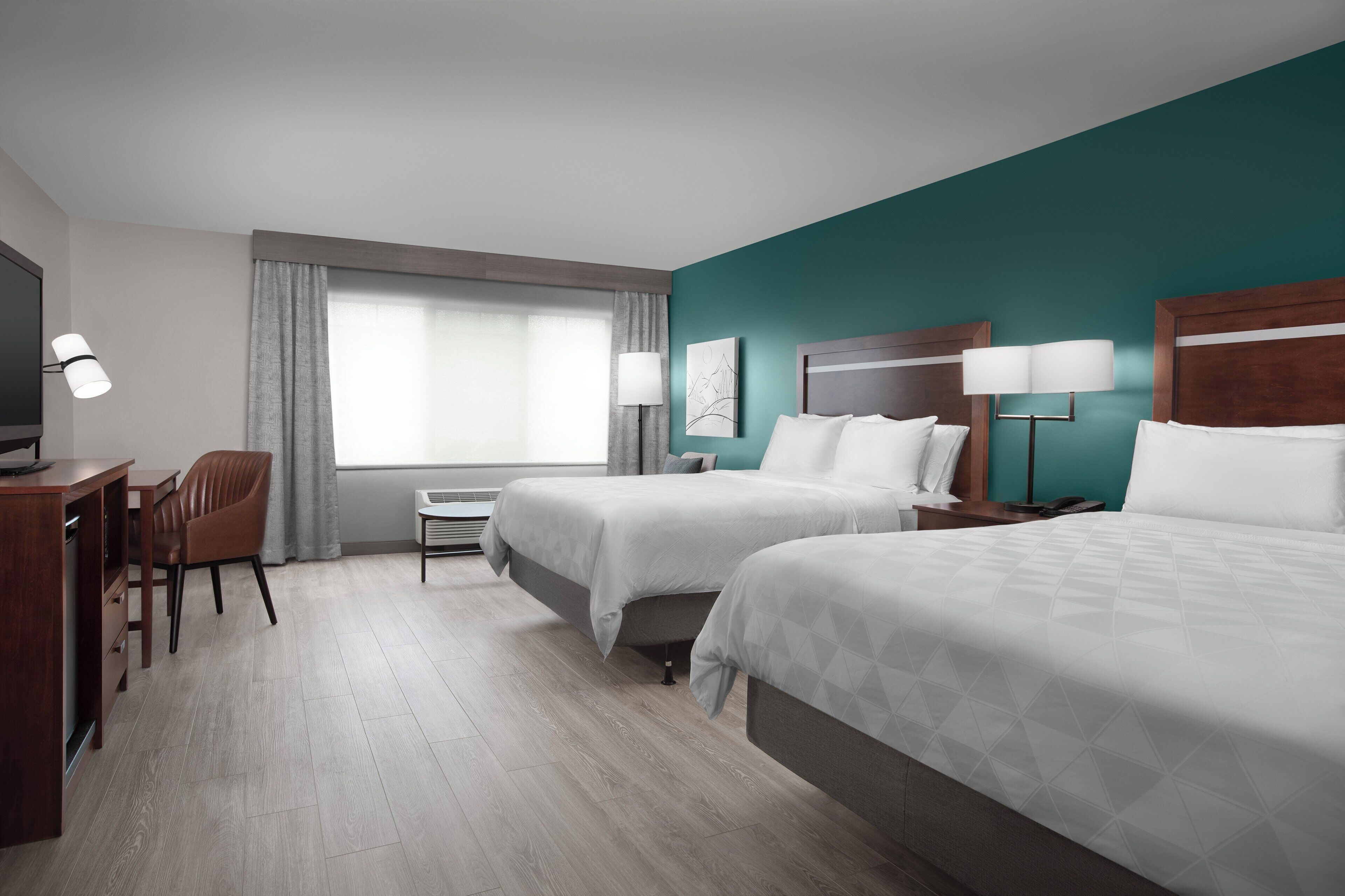 A hotel room with two beds, a desk, a chair, a TV, and a window with curtains.