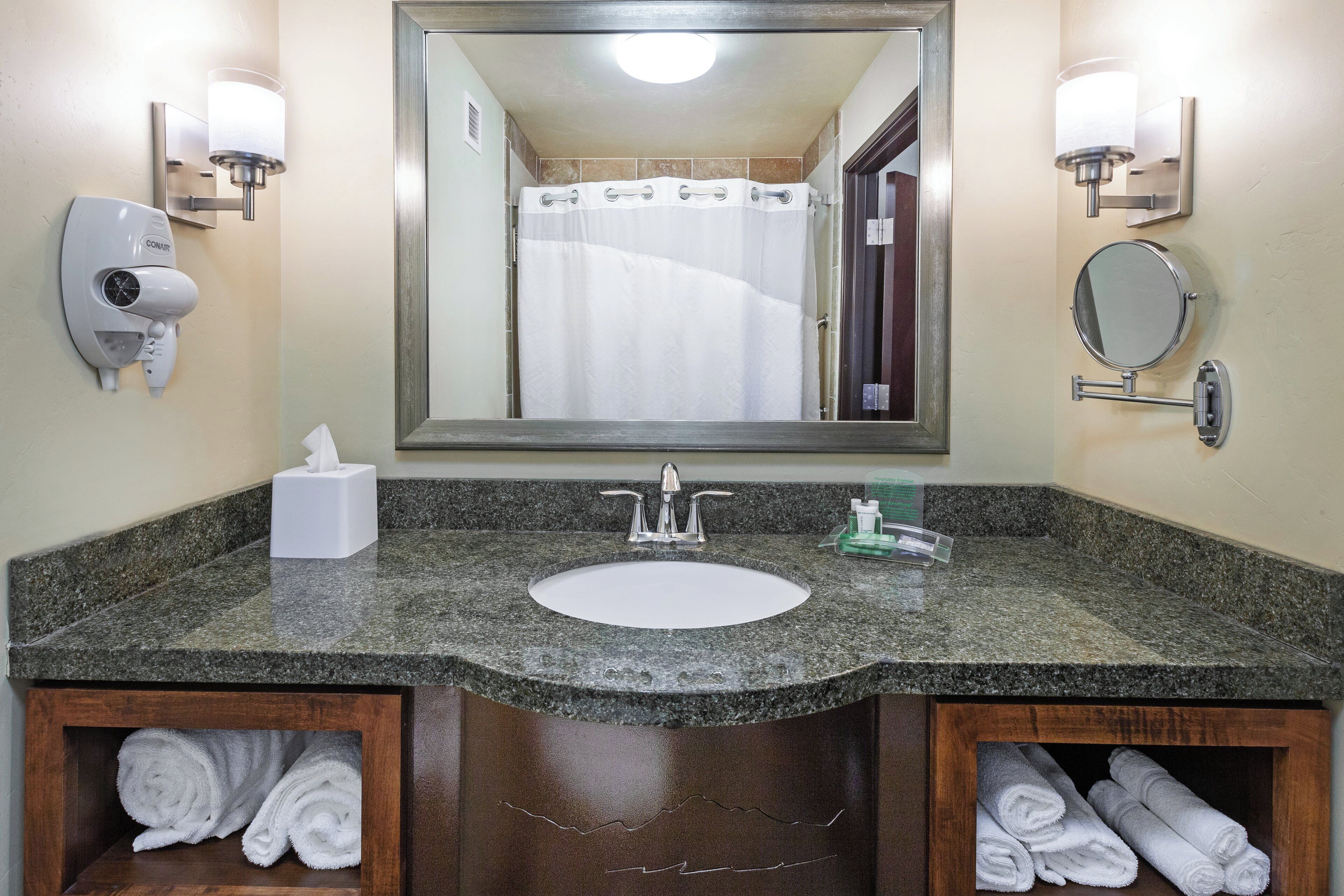 A bathroom with a granite countertop, a white sink, a mirror, a towel rack, and a hand dryer.