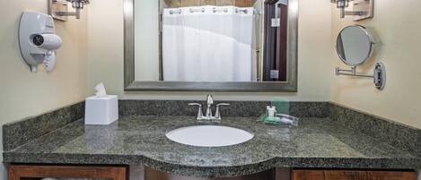 A bathroom with a granite countertop, a white sink, a mirror, a towel rack, and a hand dryer.