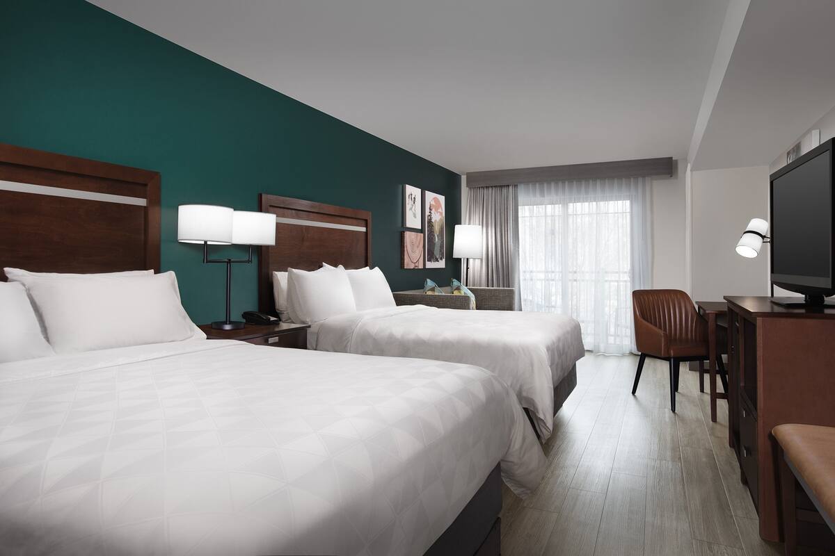 Habitación de hotel con dos camas, un escritorio, una silla, un televisor y una ventana con cortinas.