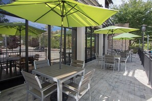 An outdoor patio area with tables and chairs, large umbrellas, and a view of the surrounding area.