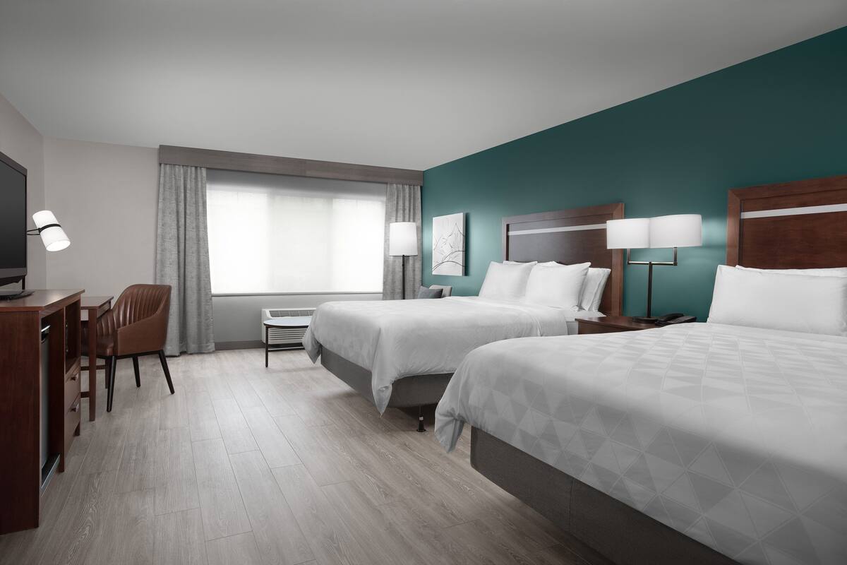 Una habitación de hotel con dos camas, un escritorio, una silla y un televisor.