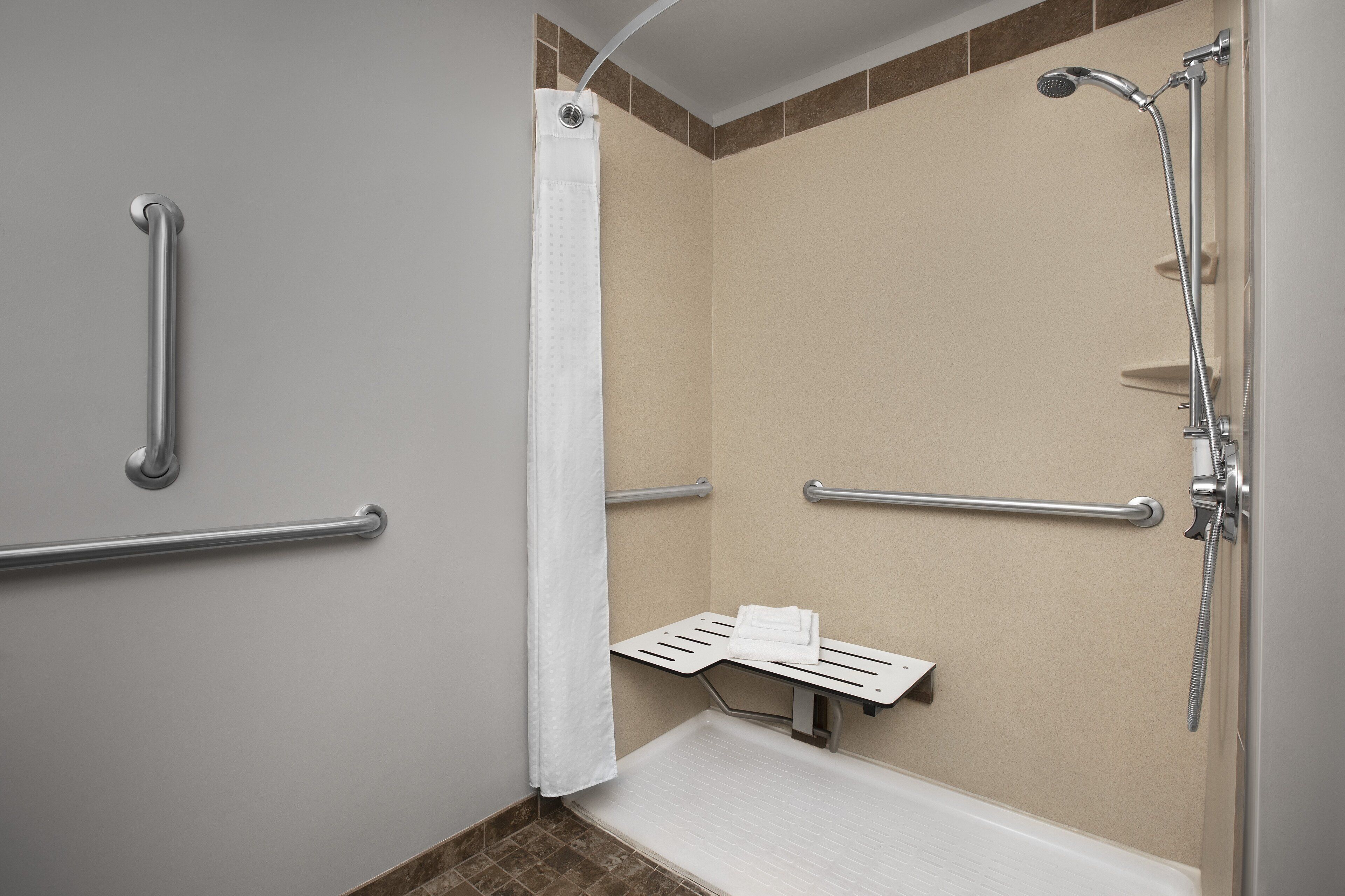 Ein Badezimmer mit Dusche, Haltegriffen, Handtuchhalter und einer Sitzbank.